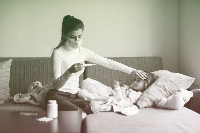 Mother wearing face protection mask at home and measure a temperature on her sick child