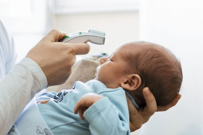 An image of a mother measuring her baby's temperature with a thermometer.