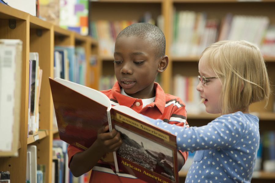 Boy and girl classmates sharing book about famous African-Americans in library