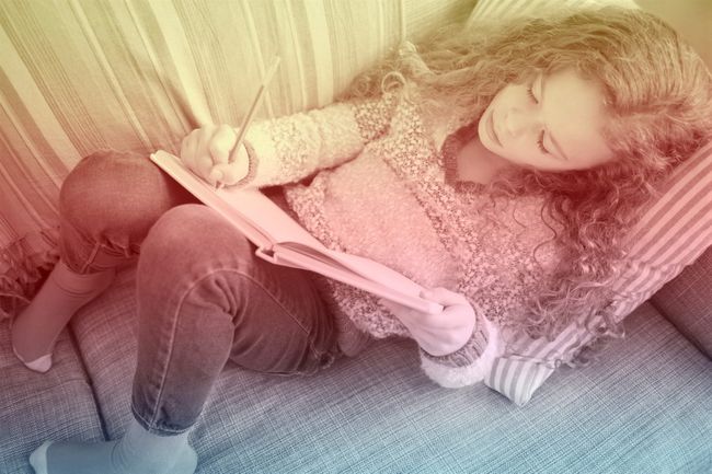 Girl lying on sofa and writing in notebook