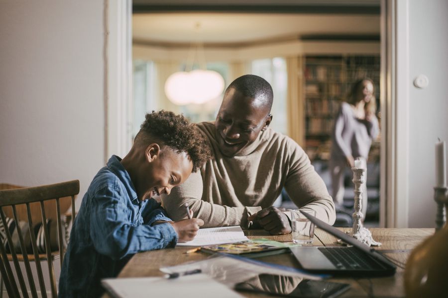 Side view of smiling son writing while studying by father over table at home