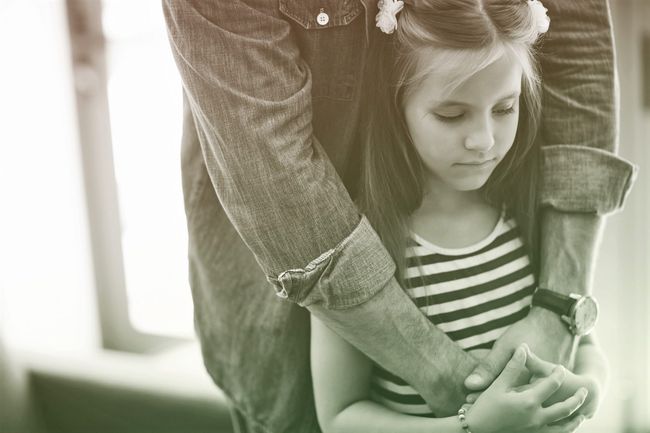 girl standing with fathers arms wrapped around her