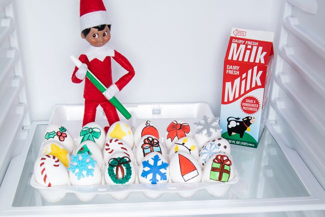 Elf on the shelf stands in refrigerator with marker and eggs decorated for Christmas