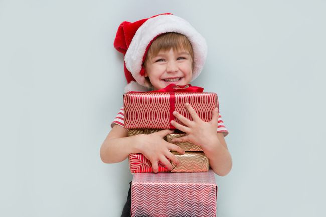 An image of a child holding presents wearing a Santa hat.