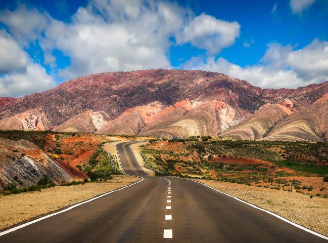 concrete road near brown mountain under blue sky