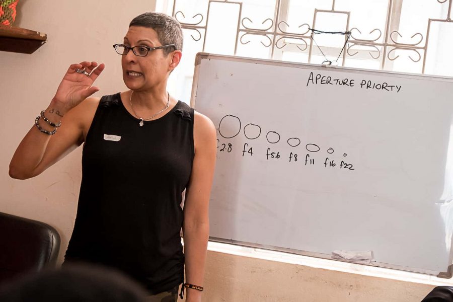 Amina Mohamed of Triple F Photo Tours stands beside a whiteboard teaching a photography class on aperture