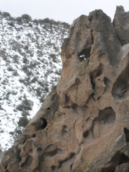 A rocky view of Bandelier National Monument with a snow-dusted hill behind