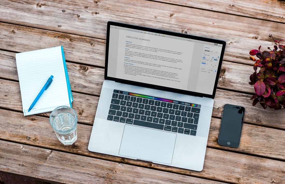 An open laptop on a wooden table with a phone and notepad