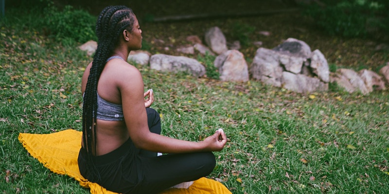 Woman meditating on a yoga mat in the grass