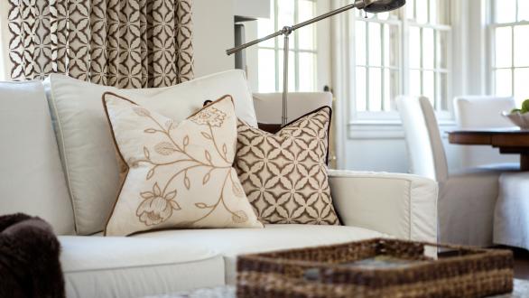 Close-up photo of a couch with warm-toned pillows and matching window treatments behind